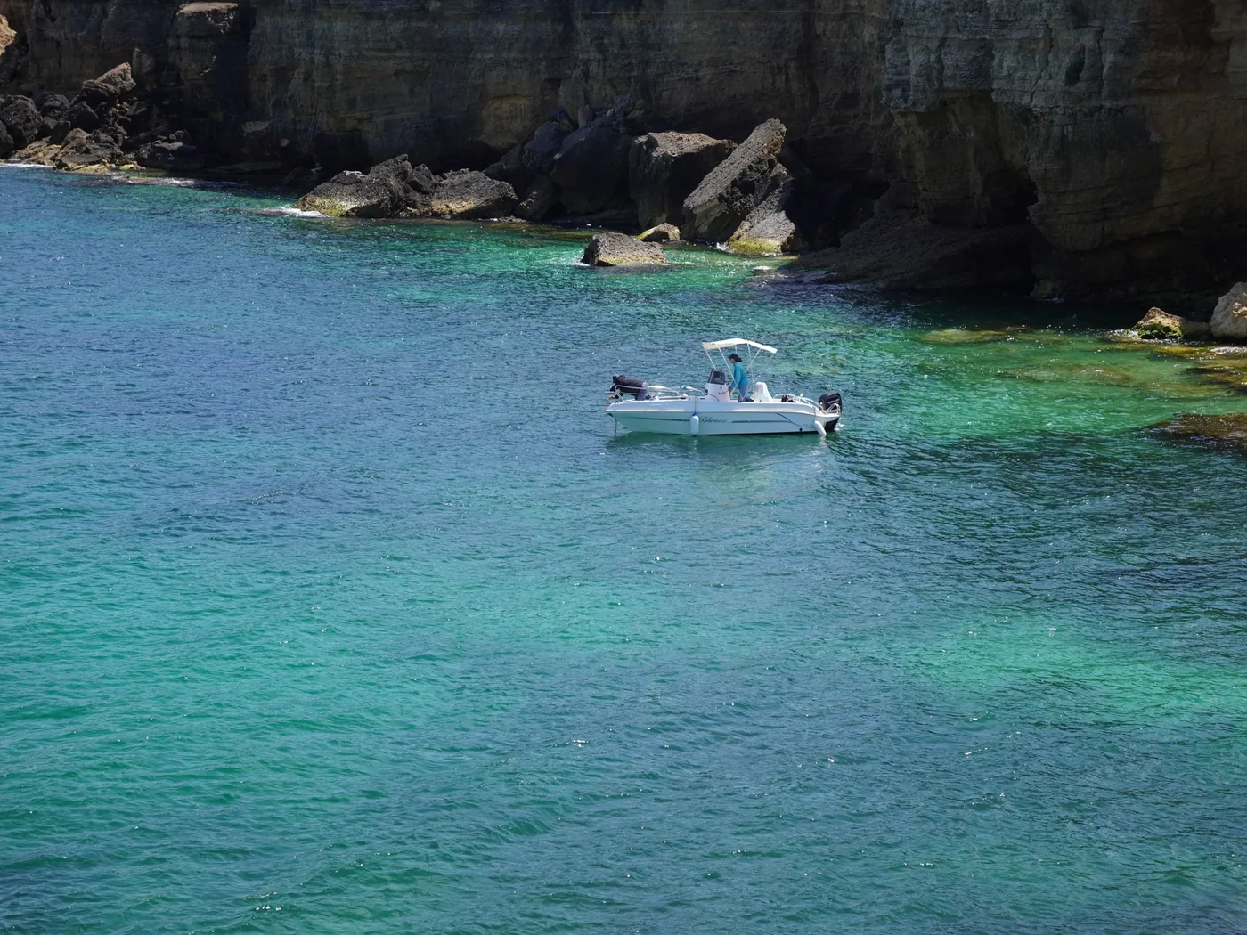 A small wooden boat on clear blue water by the Capri cliffs